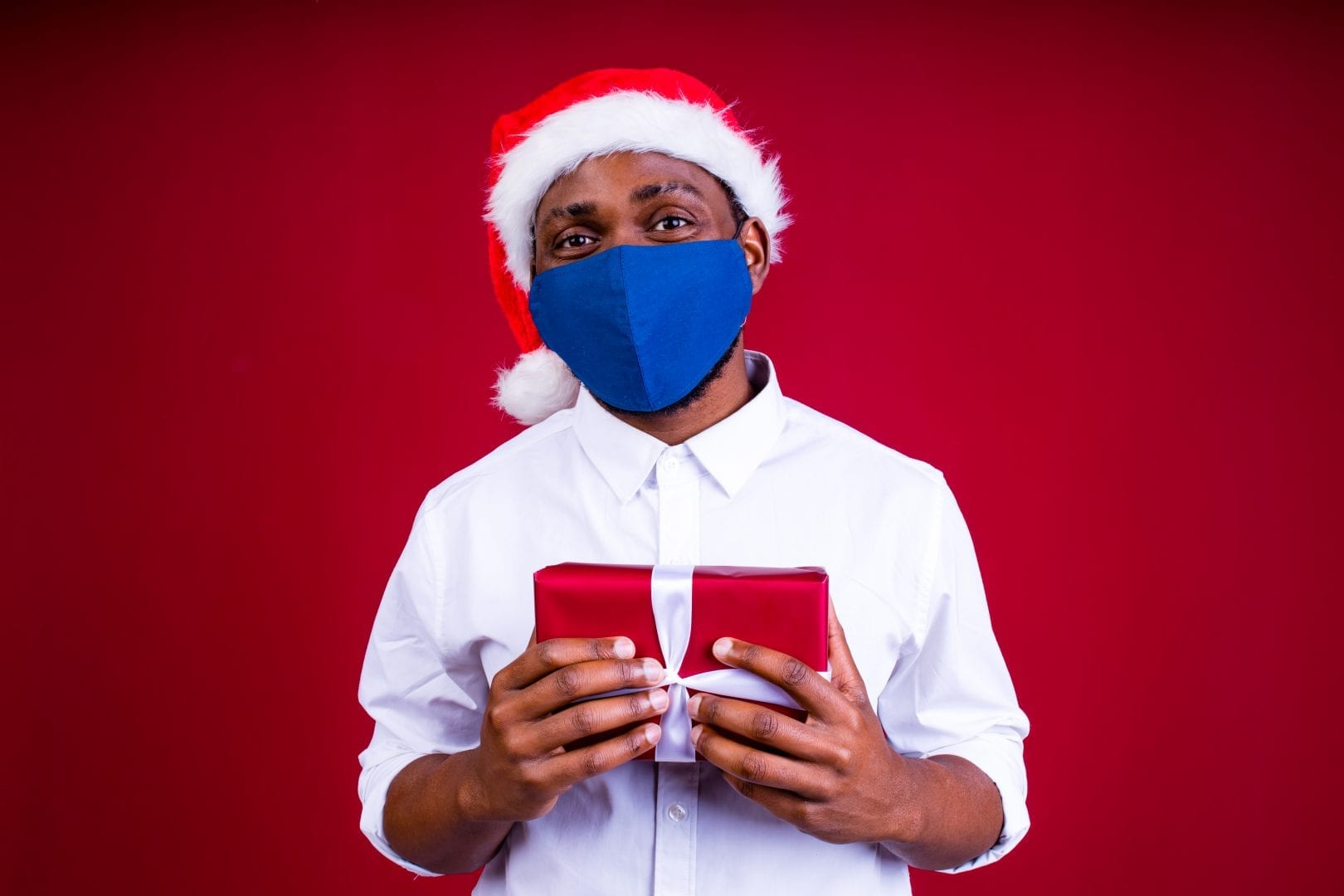 African American man in Santa's hat wearing mask in red studio background